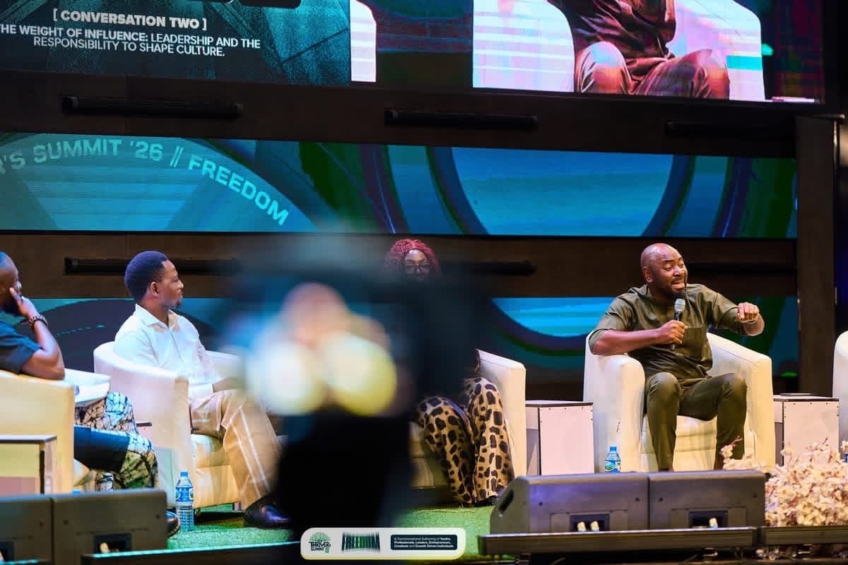Panel discussion on a stage beneath a large screen, with a speaker making a point