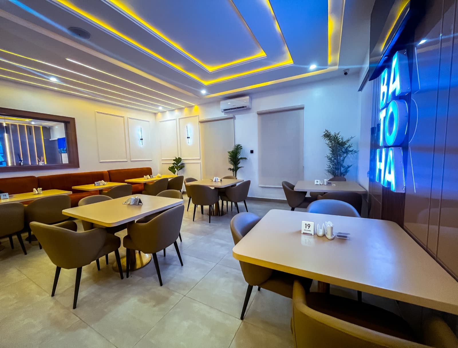 Dining lounge with a blue-lit ceiling, tables, chairs and a BATOHA neon sign