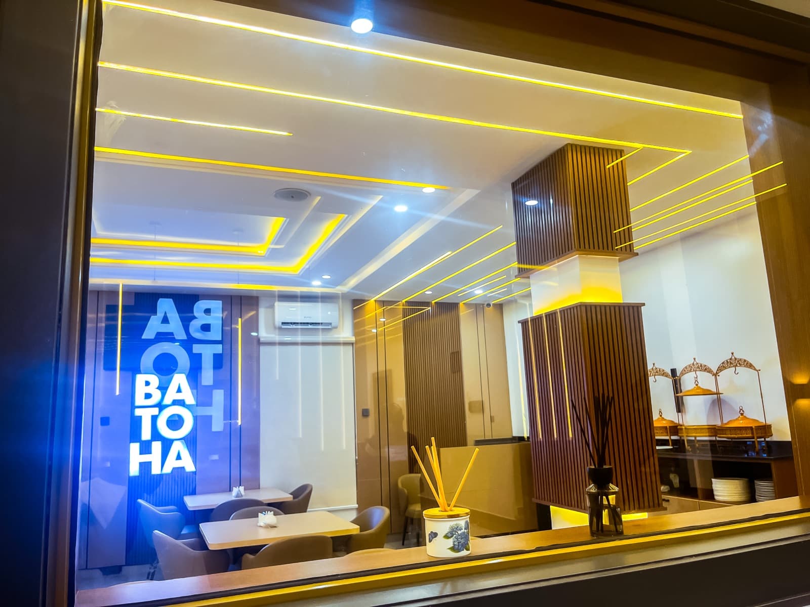 View through a window into the dining area, with a BATOHA sign and gold lighting