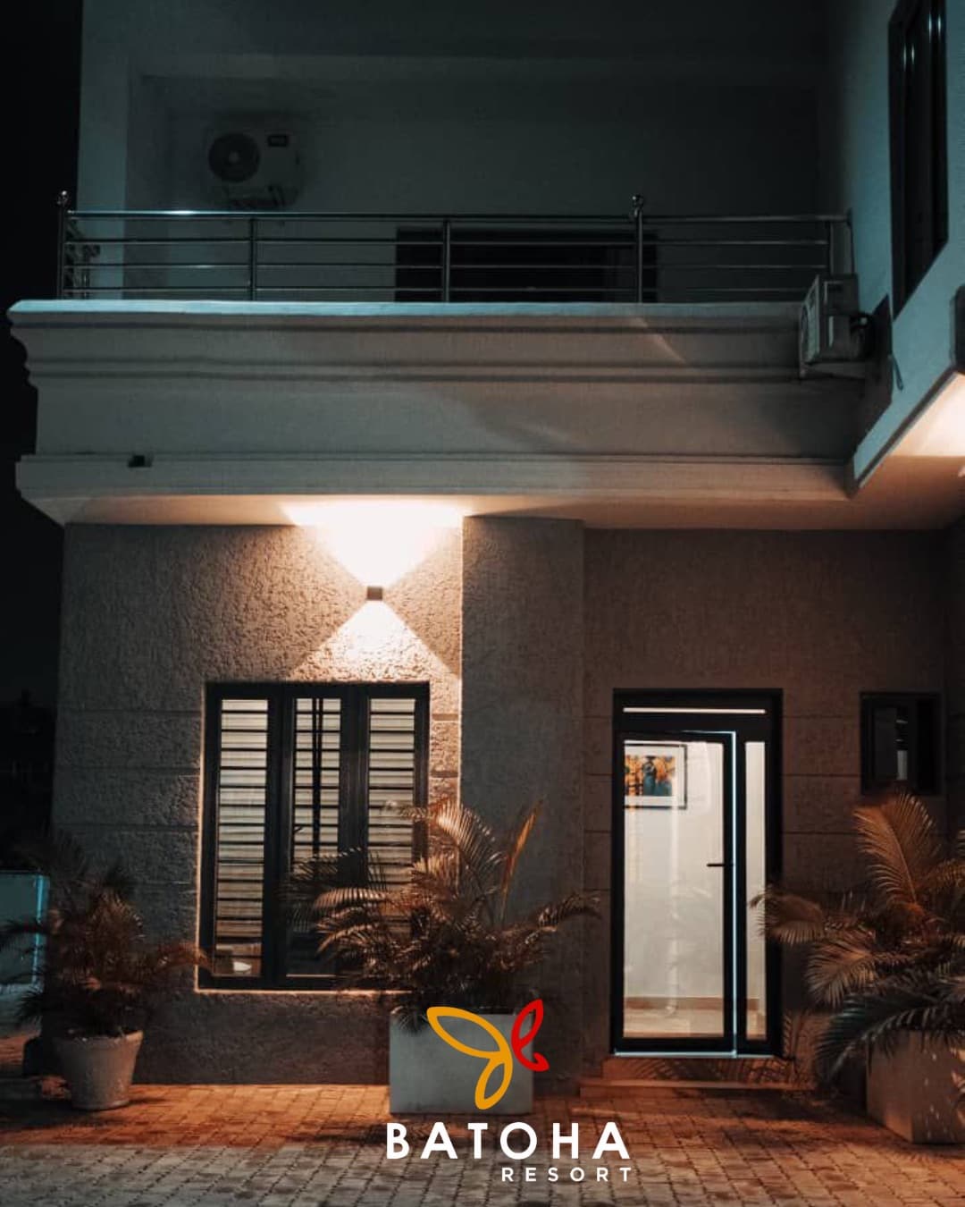 Apartment building exterior at night with warm lighting and potted plants