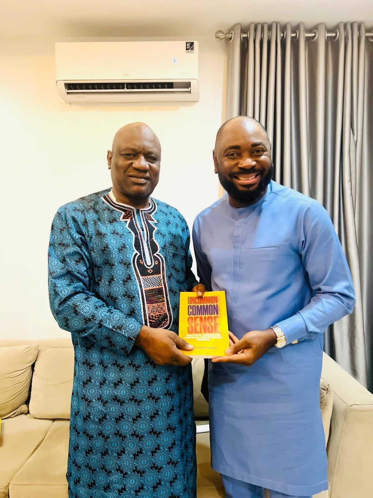 Two men in traditional attire posing with a copy of Uncommon Common Sense