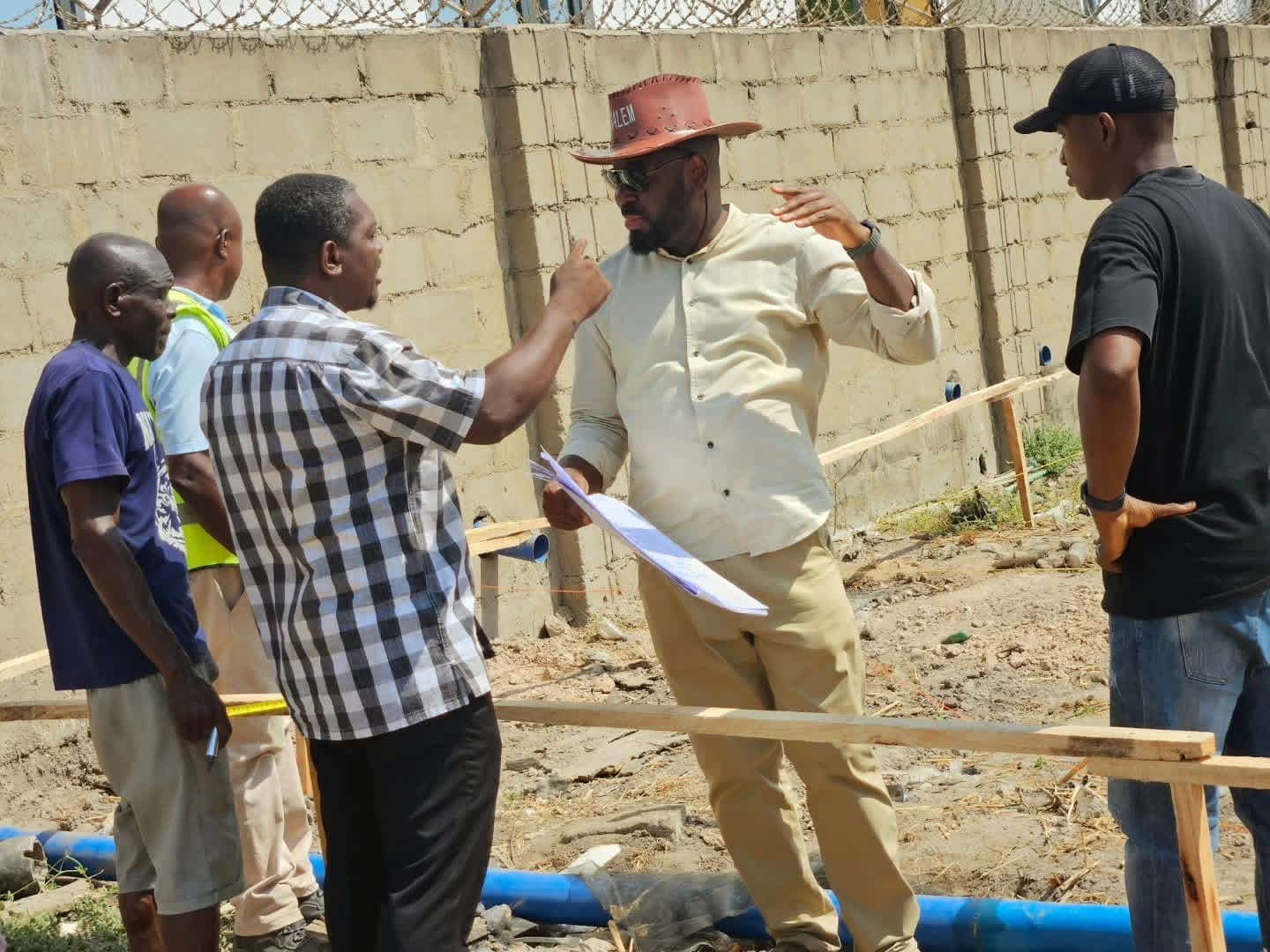 Site team in discussion, one man holding up a plan, beside a blue pipe and a block wall