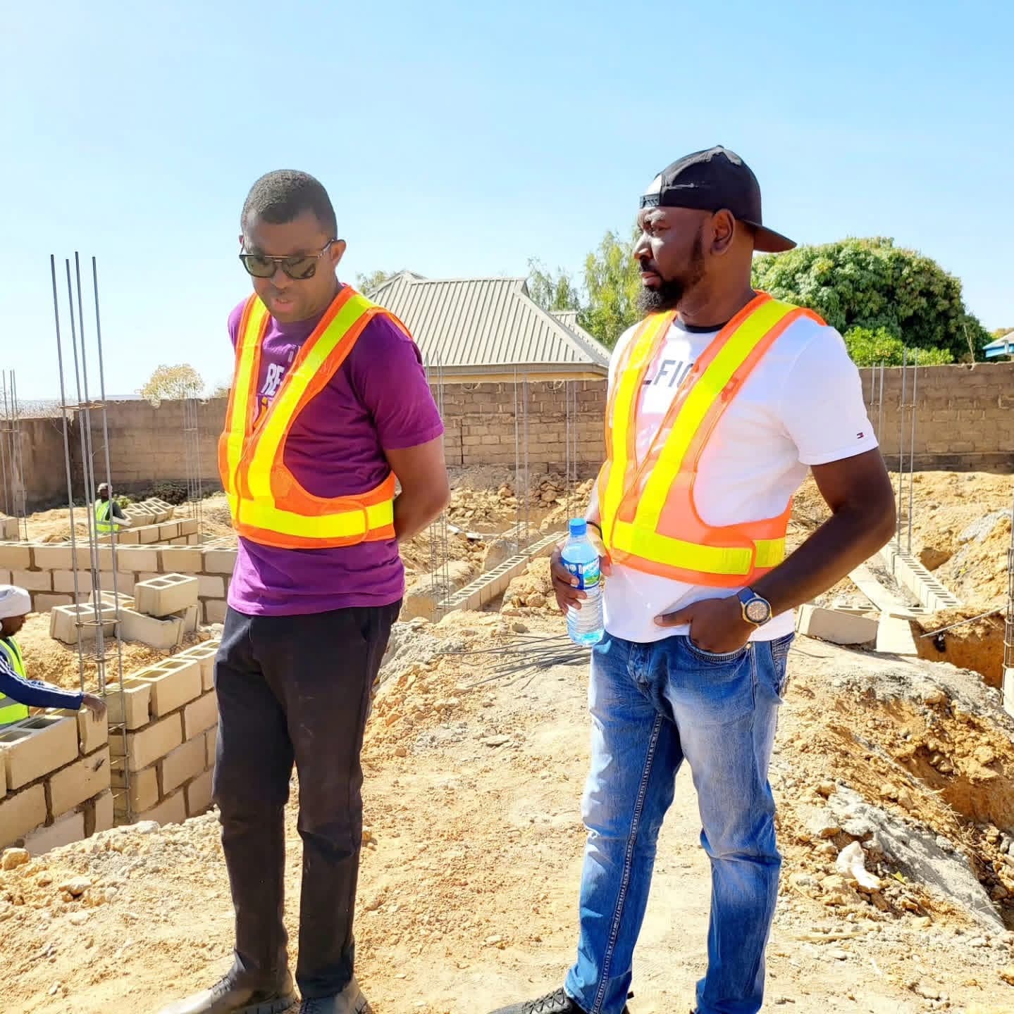 Two men in high-visibility vests on a construction site with steel reinforcement behind them