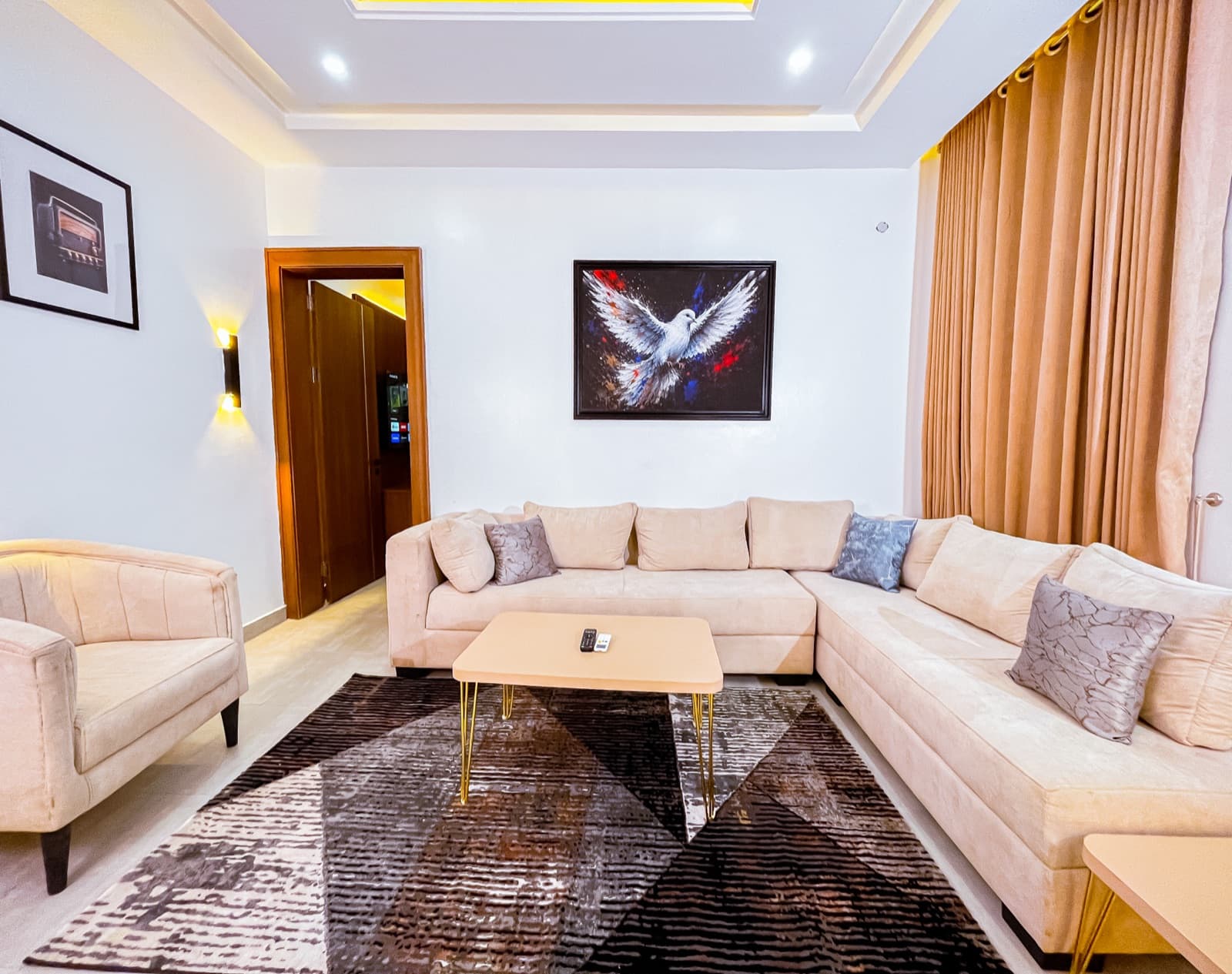 Lounge with a beige sectional, geometric rug and winged-bird artwork