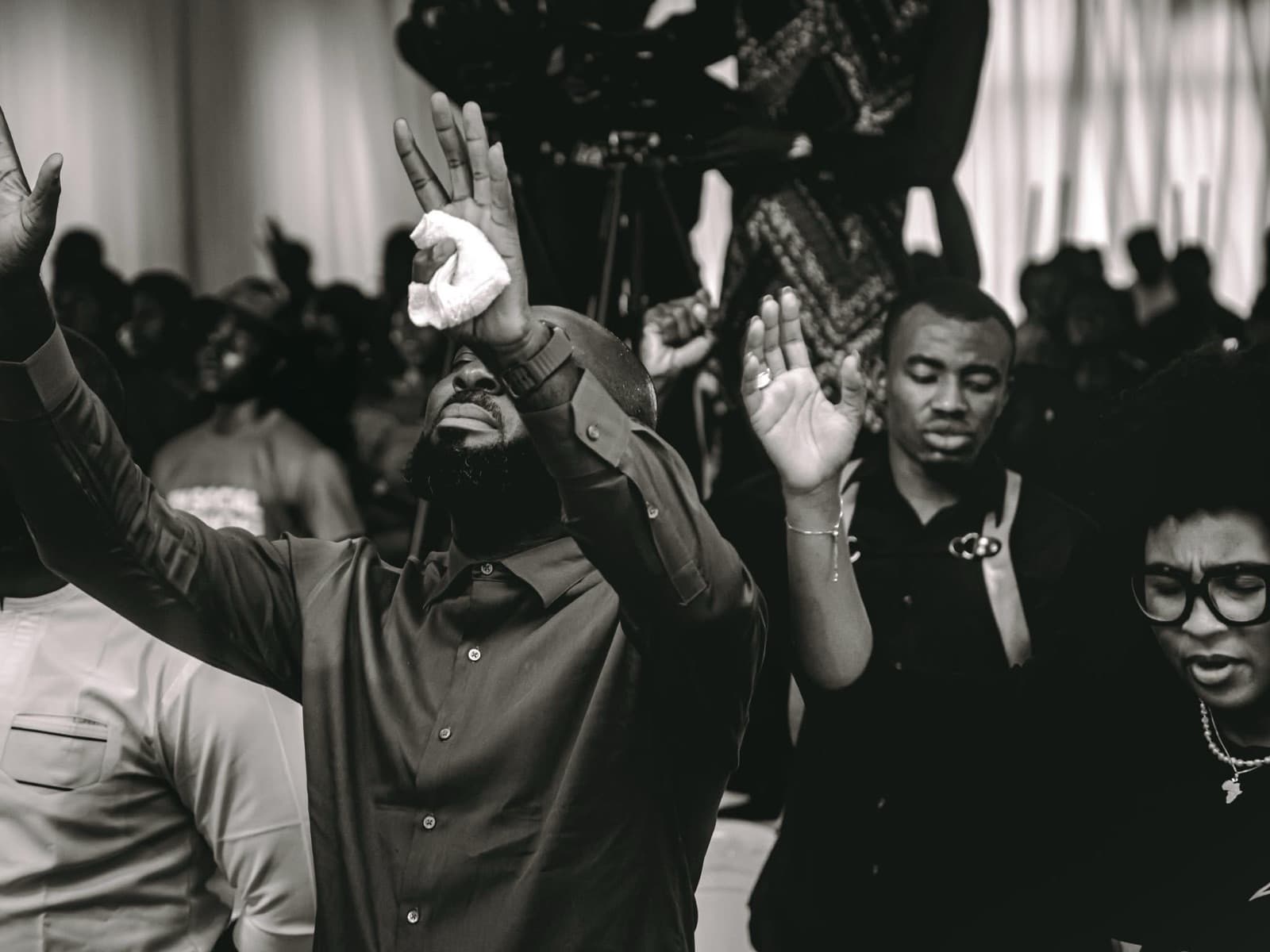 Black-and-white photo of attendees with their hands raised in prayer