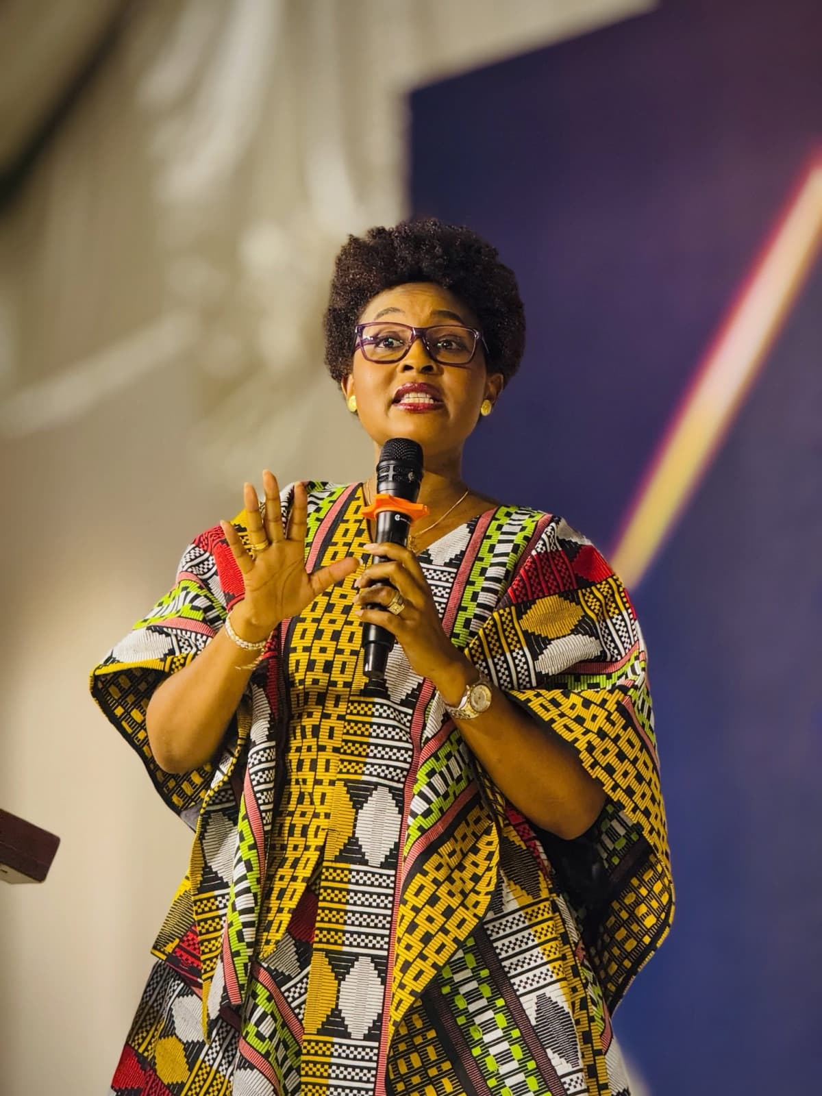 Speaker in an African-print outfit gesturing while speaking into a microphone